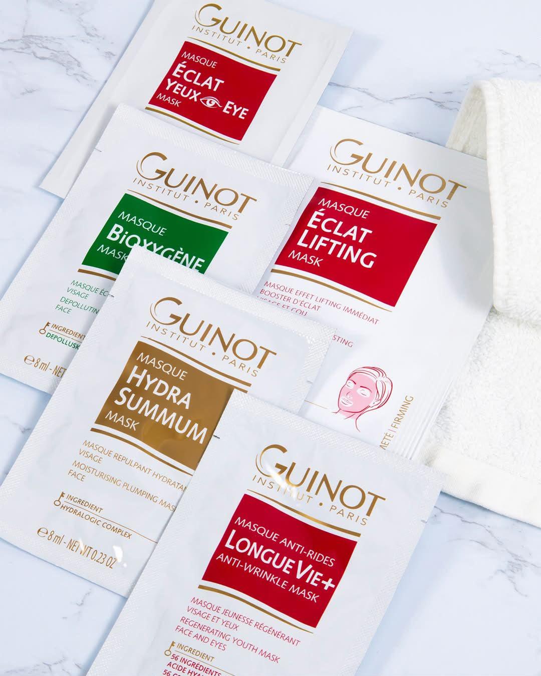 Assortment of Guintot Paris face mask sachets in red, green, and brown colors laid on a marble surface.